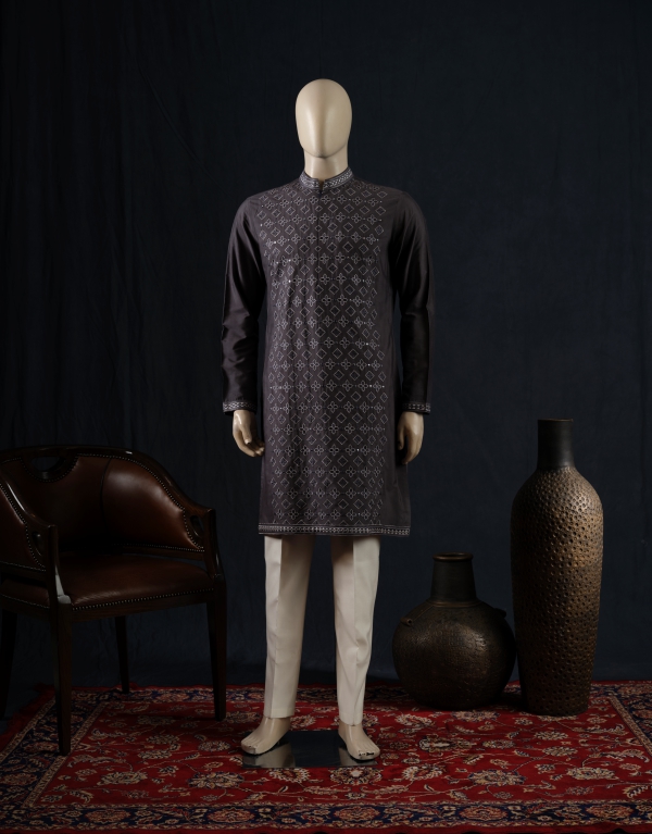 Men’s dark charcoal grey embroidered kurta paired with white churidar pants, displayed on a mannequin against a dark backdrop with traditional decor elements.