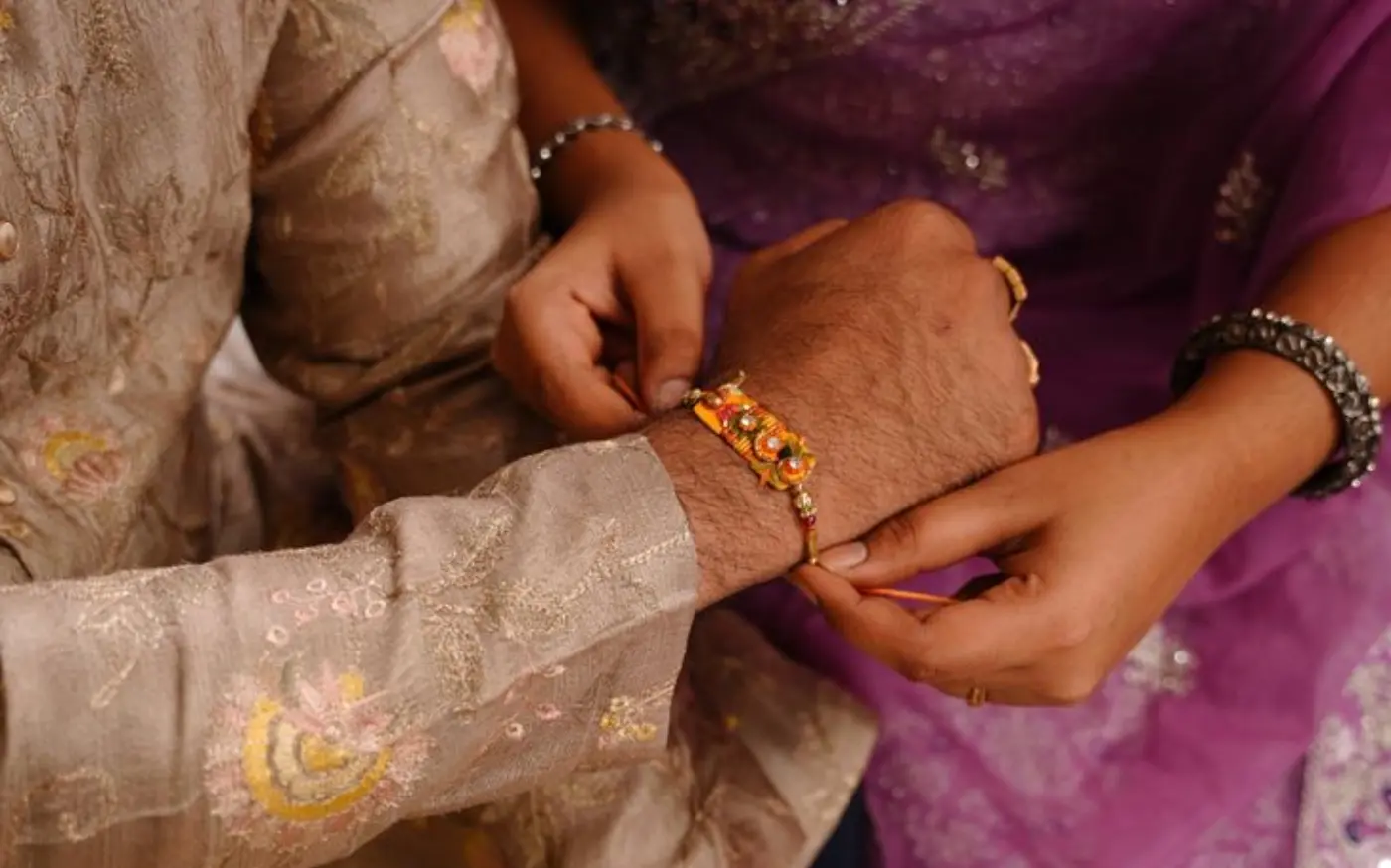 A woman tying a traditional rakhi on a man's wrist, symbolizing the Raksha Bandhan festival, with both dressed in festive ethnic attire.