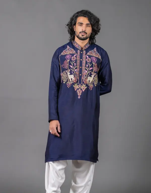 Man wearing the Lustrous Bangalore Kurta Set from The HUB Menswear, featuring a navy blue kurta adorned with intricate multicolored embroidery of florals and animals on the chest and collar, paired with white churidar pants, set against a plain grey background.